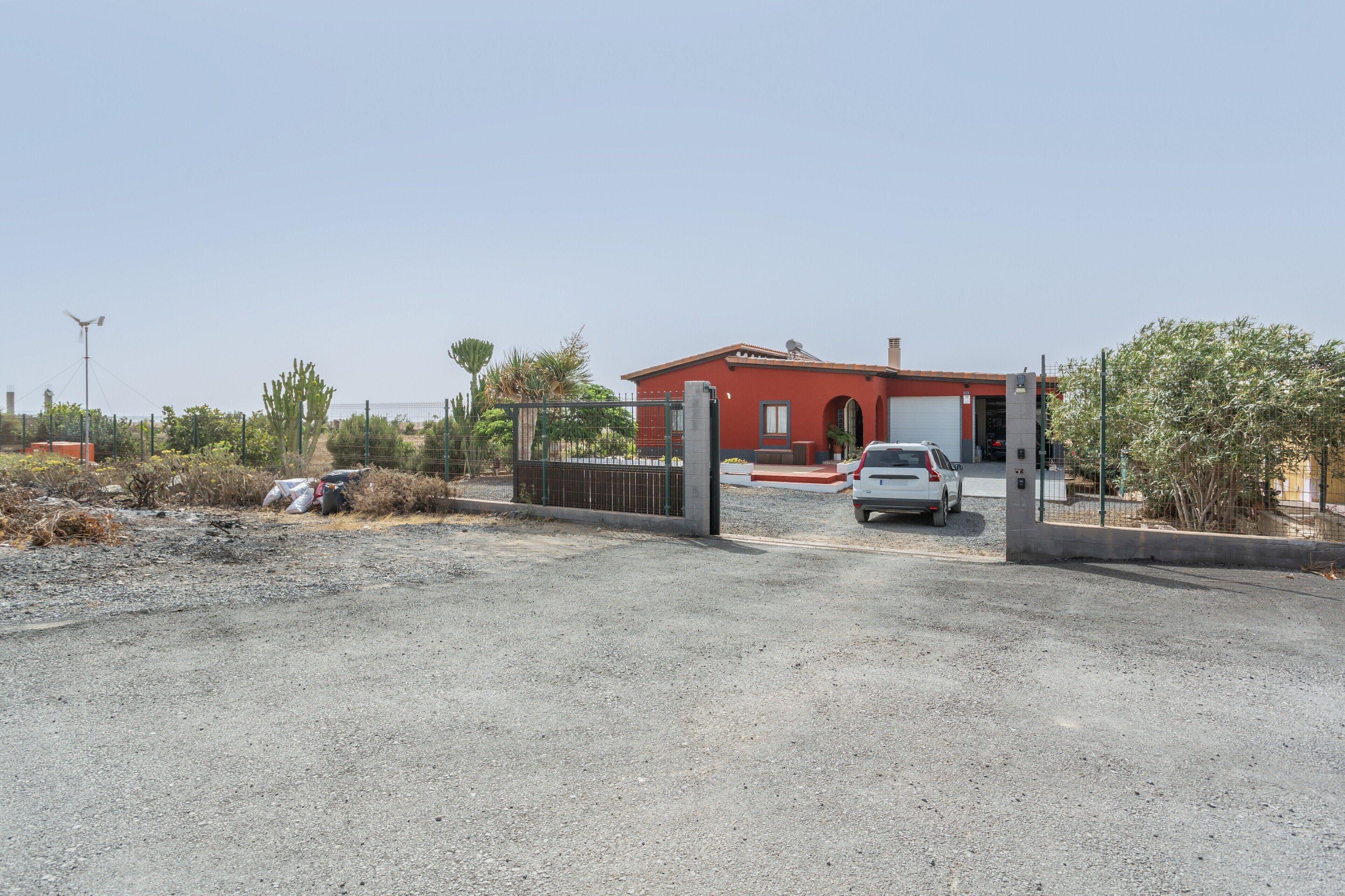 A red building with a gated entrance, a parked car, and a clear sky.