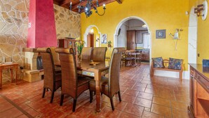 A dining area with a wooden table and chairs, a stone wall, and a yellow wall with an archway.