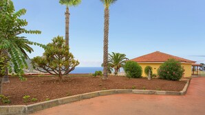 Zona enjardinada amb palmeres, un edifici groc i vista a l'oceà.