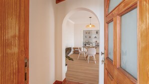 Passadís amb una porta de fusta, una porta d'arc i una zona de menjador amb cadires i taula.