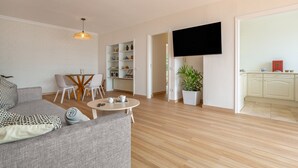 Un saló modern amb un sofà, una taula de centre, una televisió i una cuina visible a través d'una porta oberta.