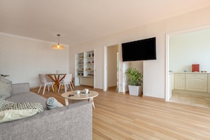 A modern living room with a sofa, a coffee table, a TV, and a kitchen area visible through an open door.
