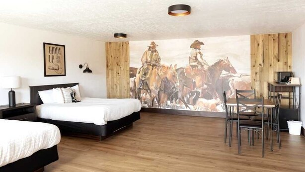A hotel room with two beds, a dining table with chairs, and a large mural of cowboys on horseback. - Double Queen Bedroom_Western Themed_Bryce Canyon (Panguitch)