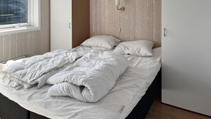 Uma cama de solteiro com roupa de cama branca num quarto com paredes de painel de madeira e uma janela.