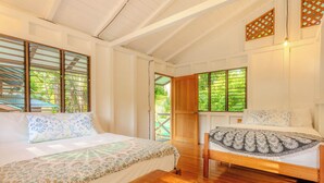 Une chambre avec deux lits, un plancher en bois et de grandes fenêtres équipées de stores en bois.