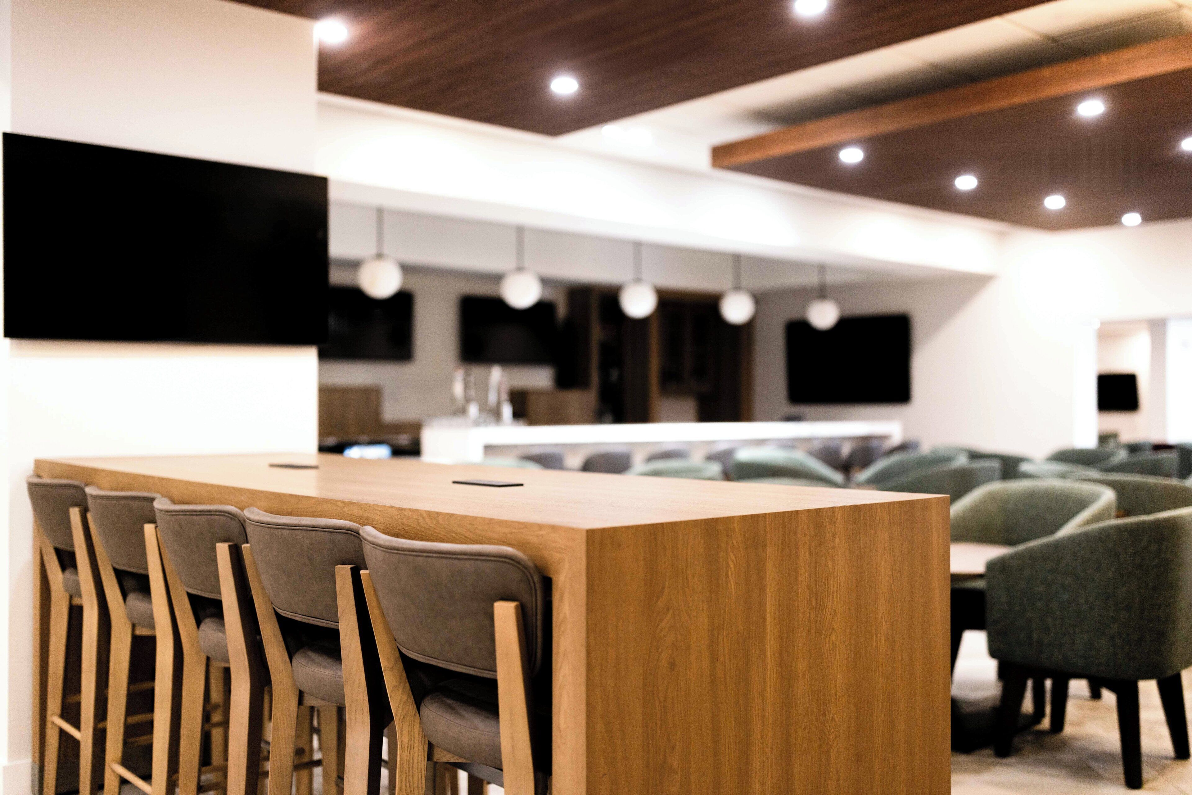Un área de bar moderna con barra de madera y sillas tapizadas grises.