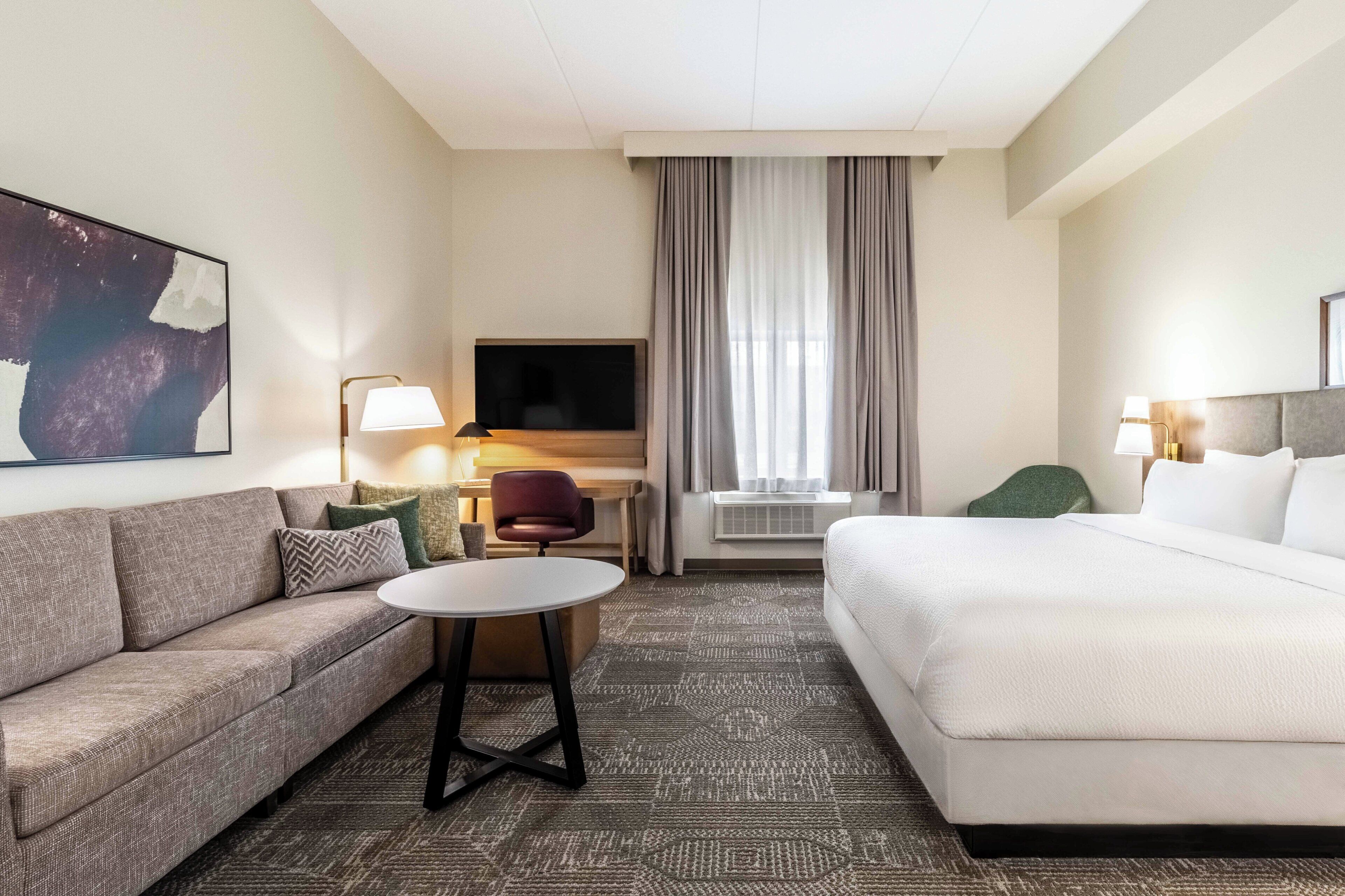 A hotel room with a sofa, a bed, a TV, a desk, and a chair.