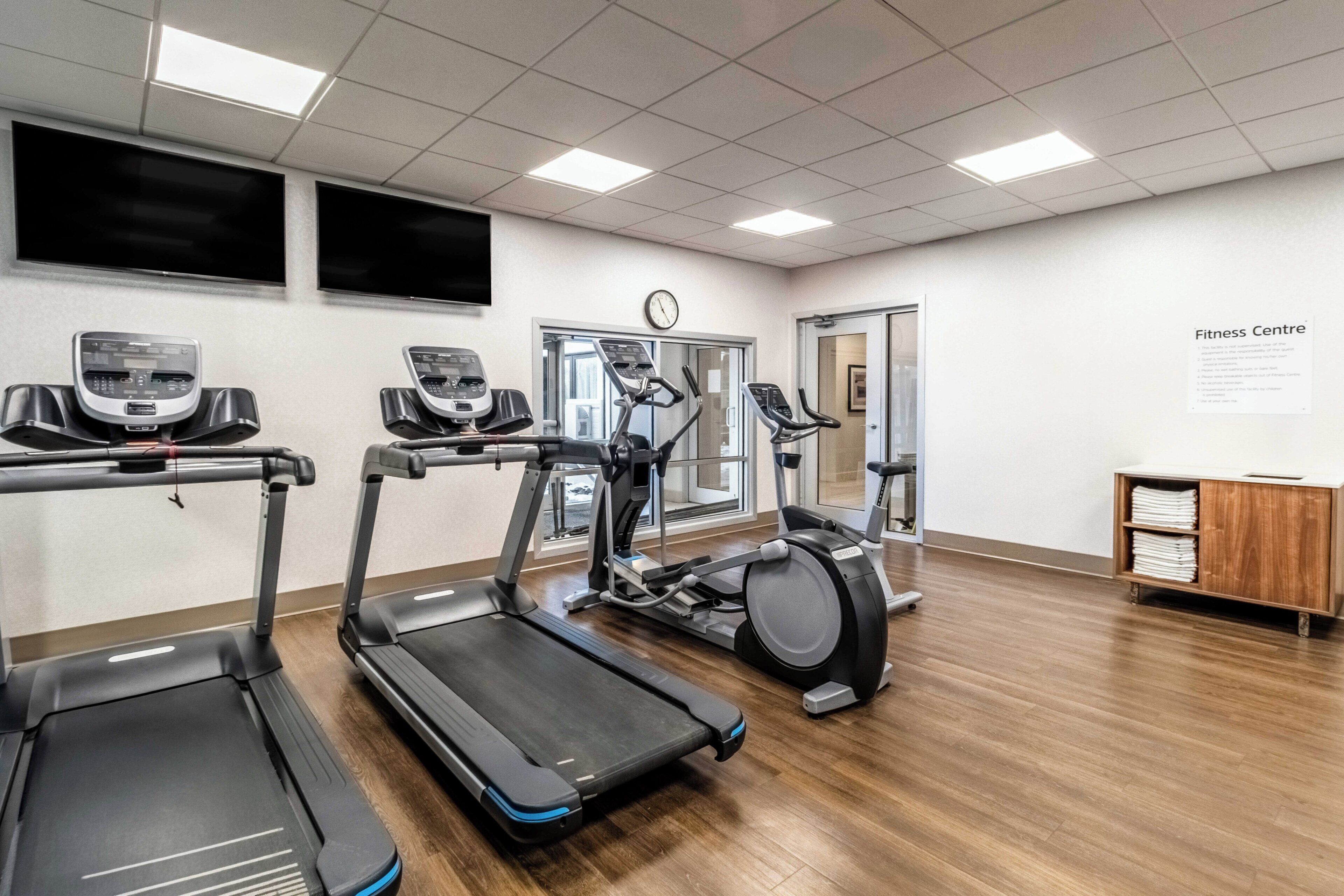 A fitness center with treadmills, elliptical machines, and a wall clock.