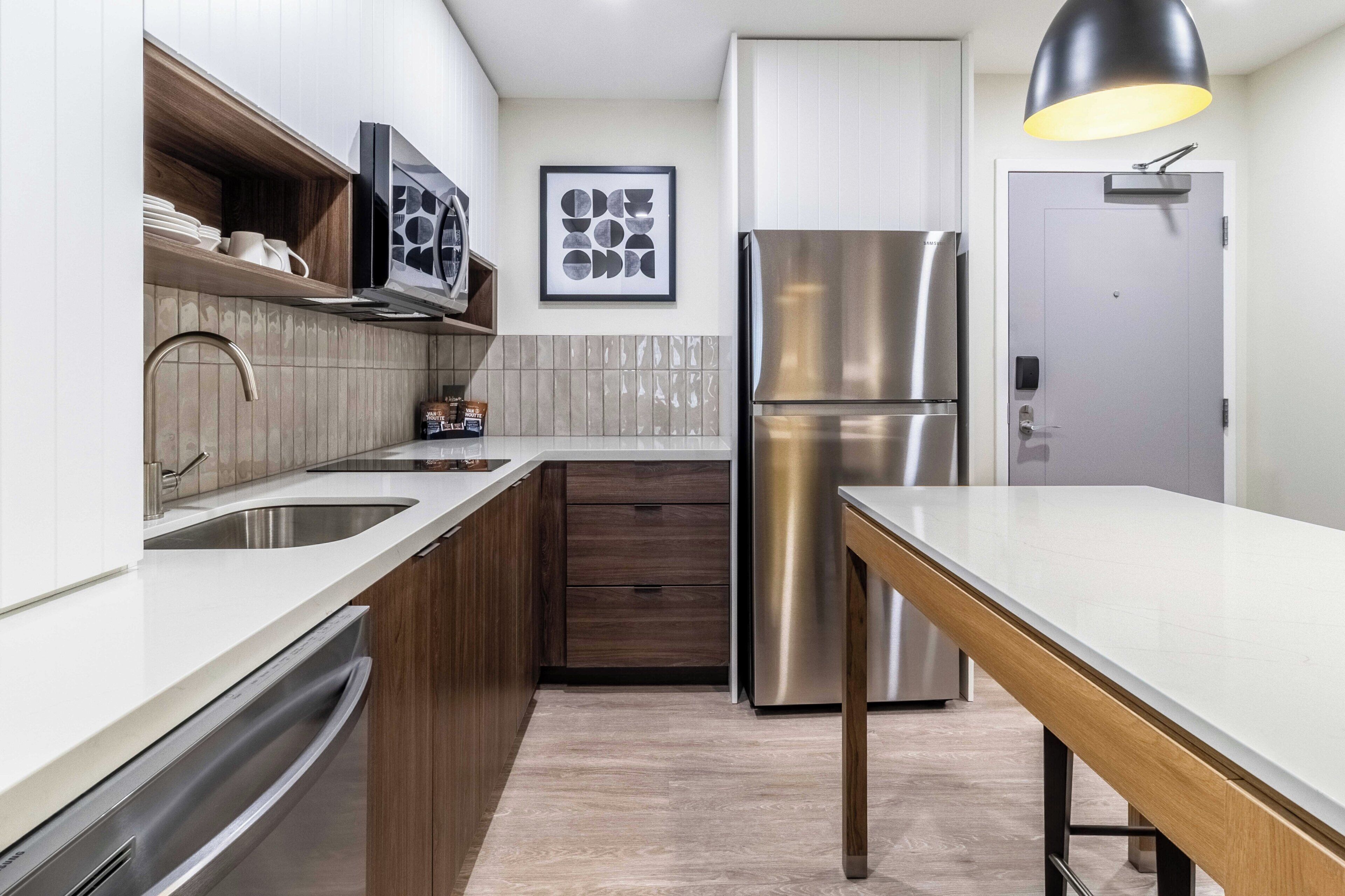 A modern kitchen with a stainless steel refrigerator, wooden cabinets, and a white countertop.