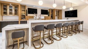 Una cocina moderna con una isla central, taburetes de bar, armarios de madera y un televisor de pantalla plana.