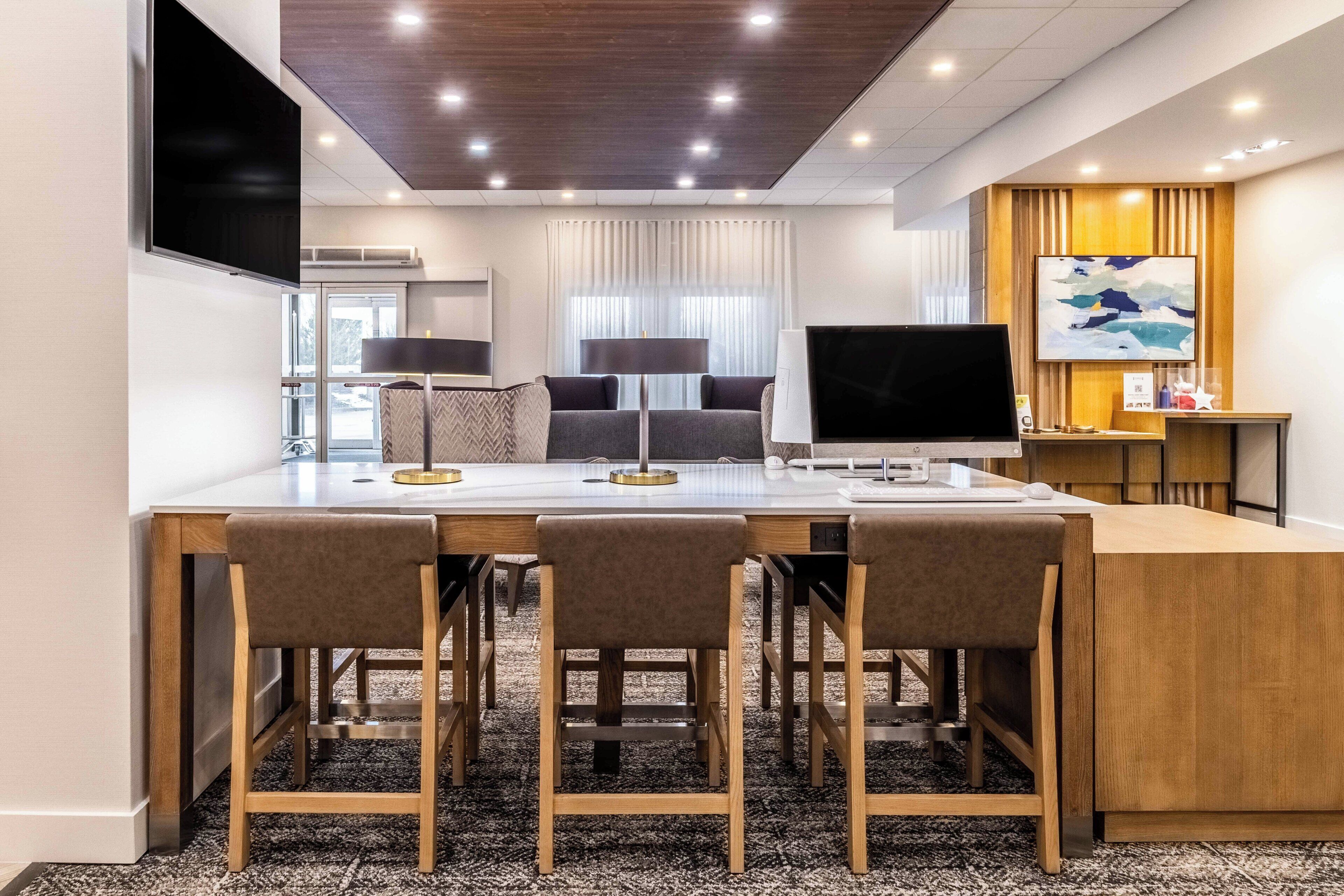 A modern hotel room with a dining area featuring a wooden table and four chairs, a flat-screen TV, and a large window with curtains.