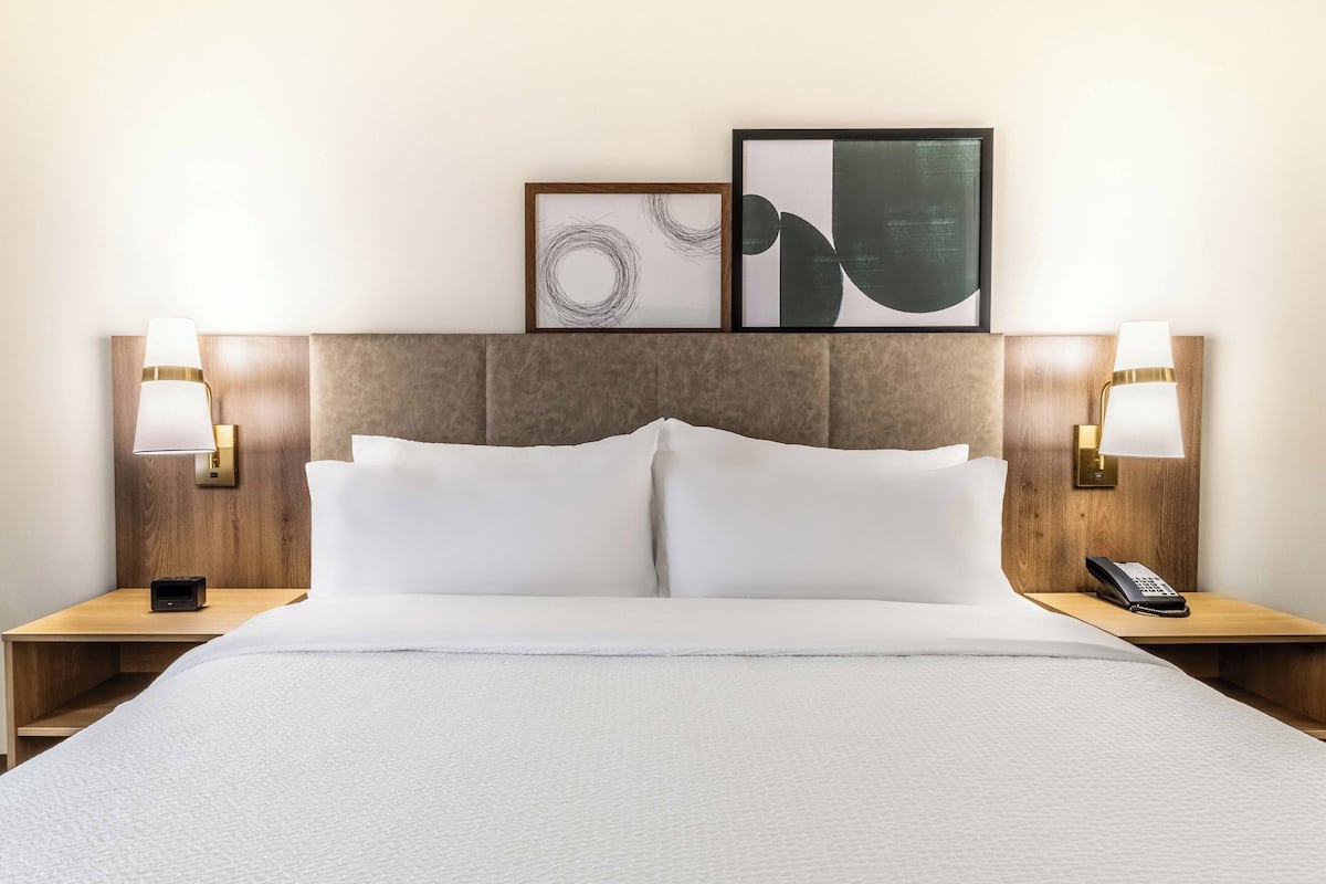 Habitación de hotel con una cama grande, dos mesitas de noche, un teléfono y dos cuadros en la cabecera.