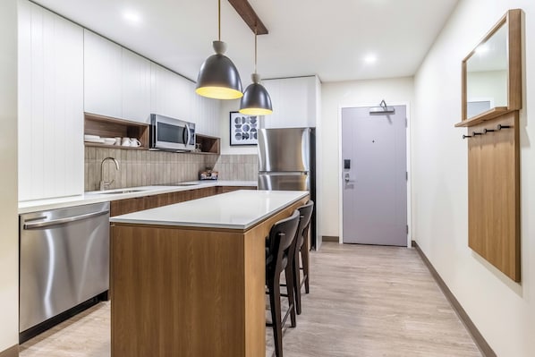 Uma cozinha moderna com uma ilha central, eletrodomésticos de aço inoxidável, iluminação pendente e armários de madeira.