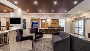 Un vestíbulo moderno de hotel con mostrador de recepción, zona de estar y una gran pantalla de televisión.
