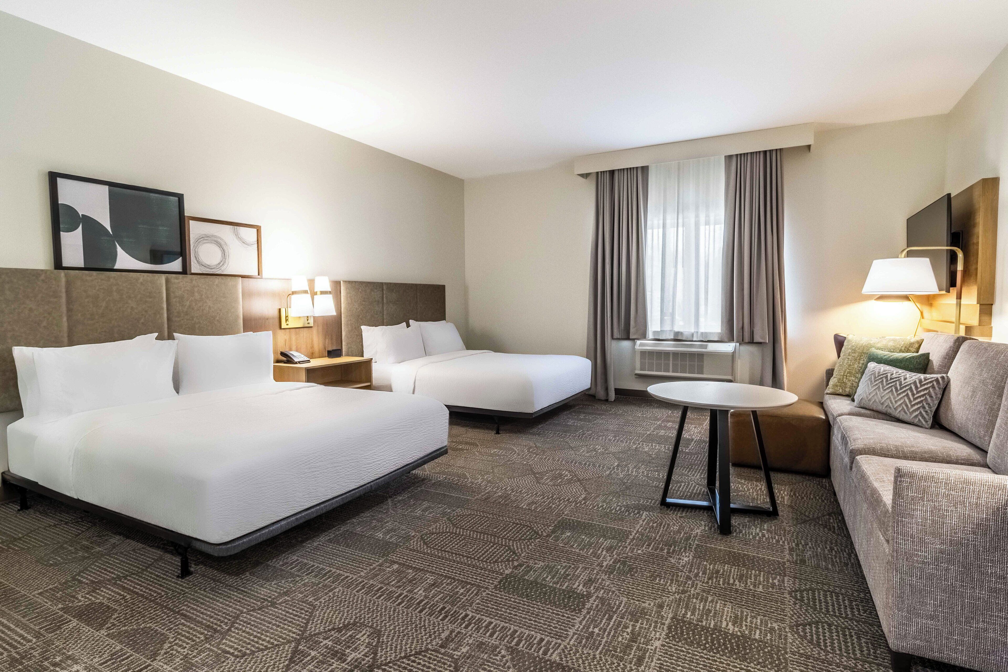 Habitación de hotel con dos camas, un sofá, una mesita, un televisor y una ventana con cortinas.