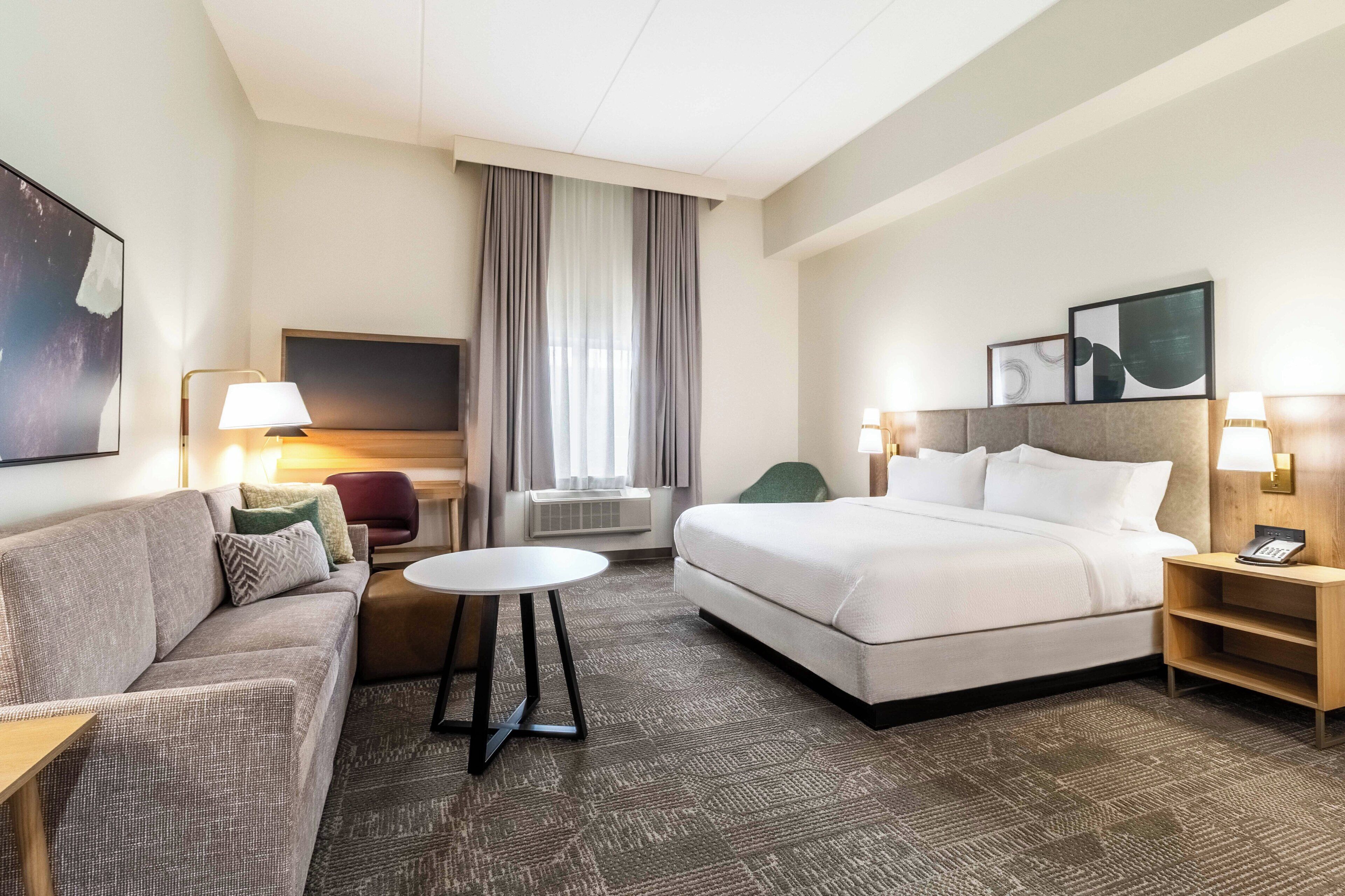 Una habitación de hotel con cama, sofá, una mesita y un escritorio con lámpara.