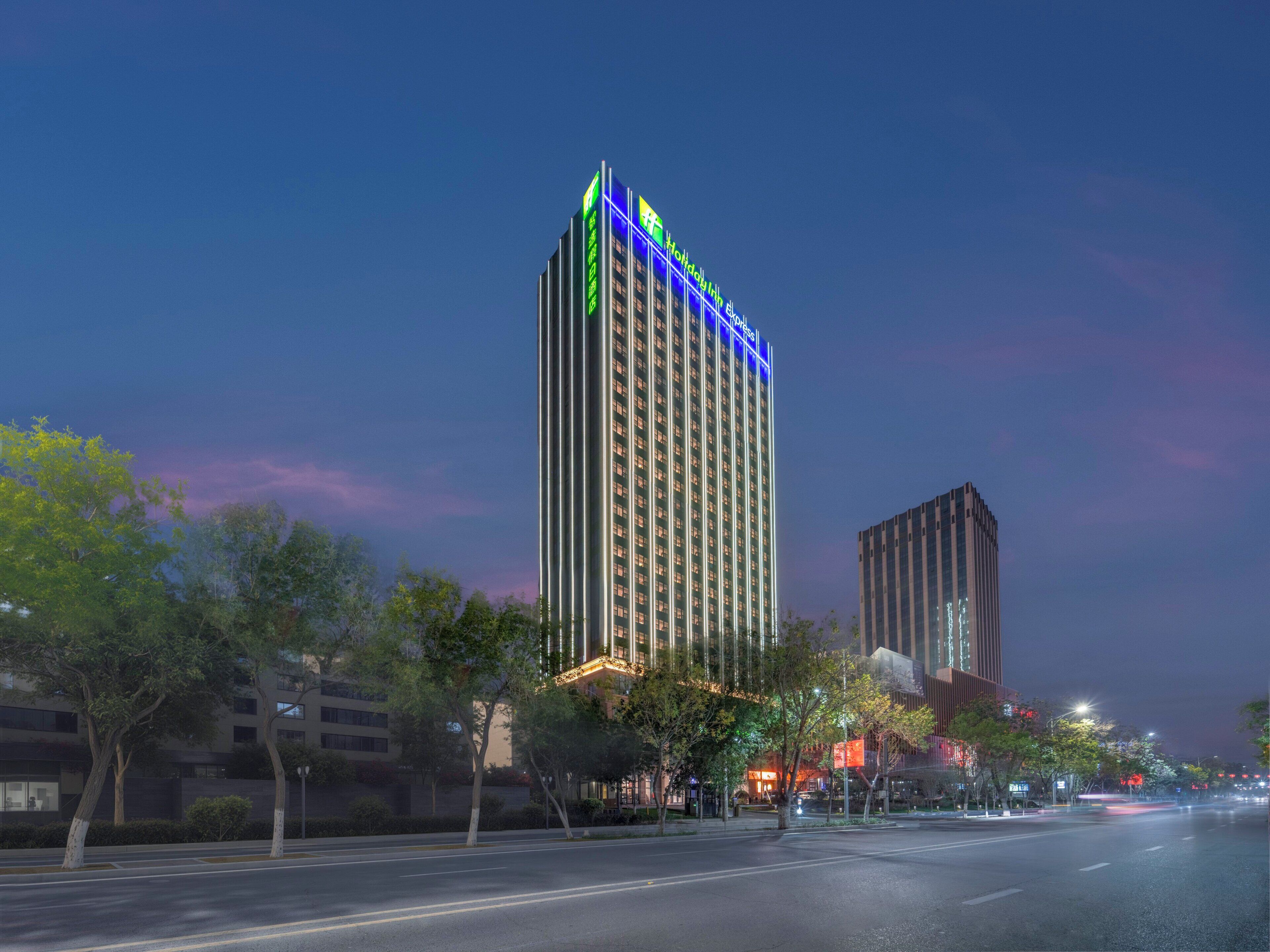 A high-rise hotel with a prominent sign at the top, surrounded by trees and a clear sky.