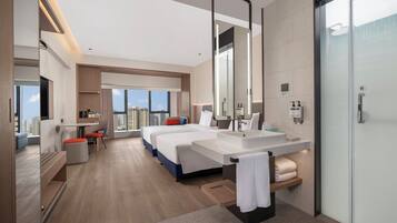 Une chambre d’hôtel moderne dotée d’un grand lit, d’un coin salon séparé, d’une grande salle de bain avec un miroir et d’une vue sur la ville.