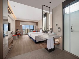 Habitación de hotel moderna con una cama grande, un área de estar separada, un baño espacioso con espejo y vistas a la ciudad.