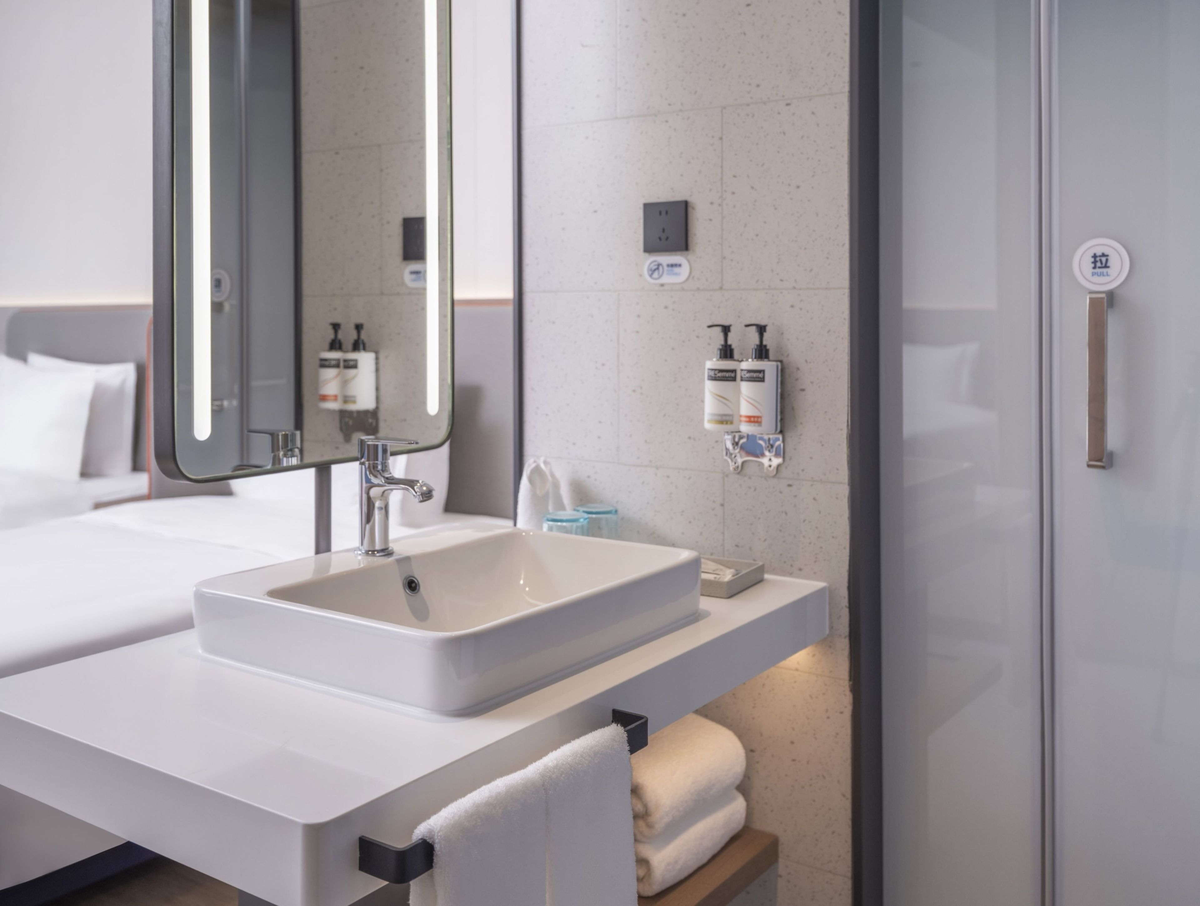 A modern bathroom with a large mirror, a white sink, and two hand soap dispensers.