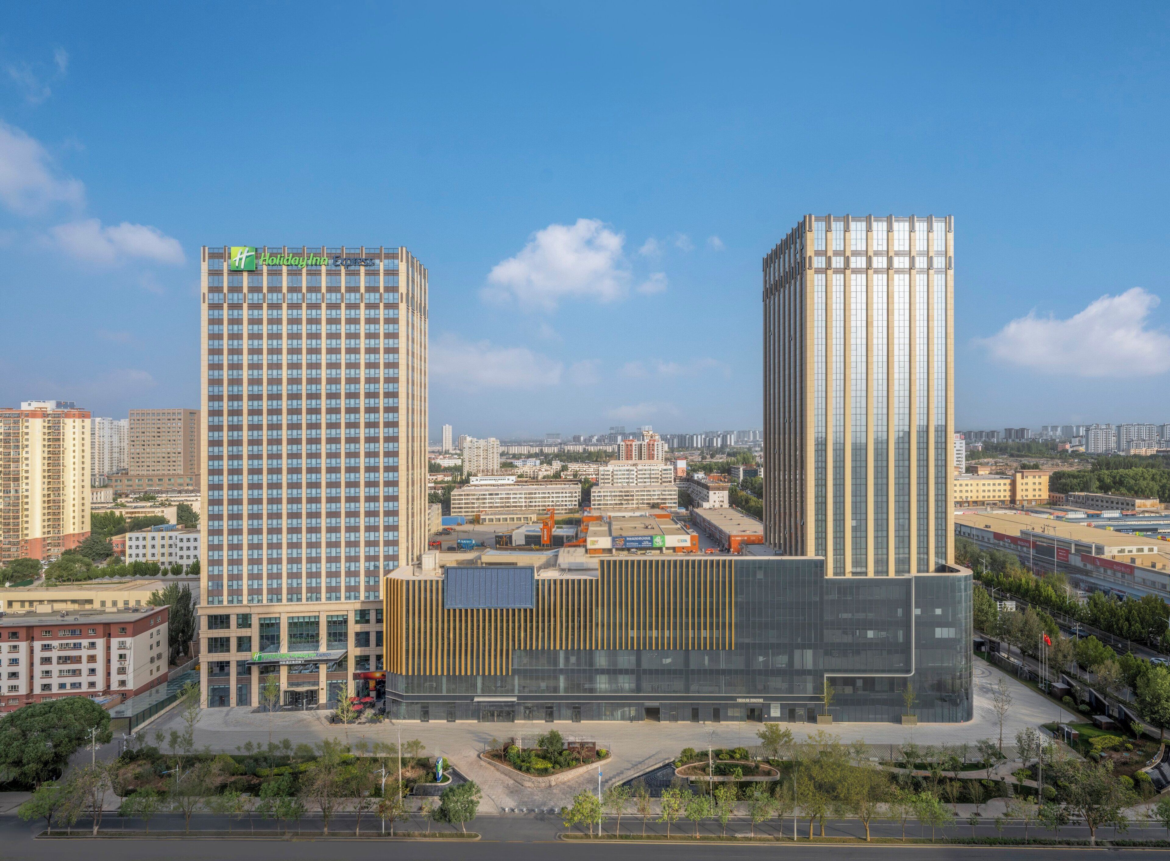 A modern hotel with a prominent 'Holiday Inn' sign, surrounded by other high-rise buildings and a clear sky.