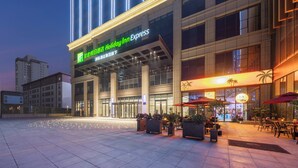 A Holiday Inn Express hotel with a modern facade, large glass windows, and outdoor seating area with umbrellas. - Holiday Inn Express Aksu by IHG (Aksu)
