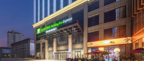A Holiday Inn Express hotel with a modern facade, large glass windows, and outdoor seating area with umbrellas.