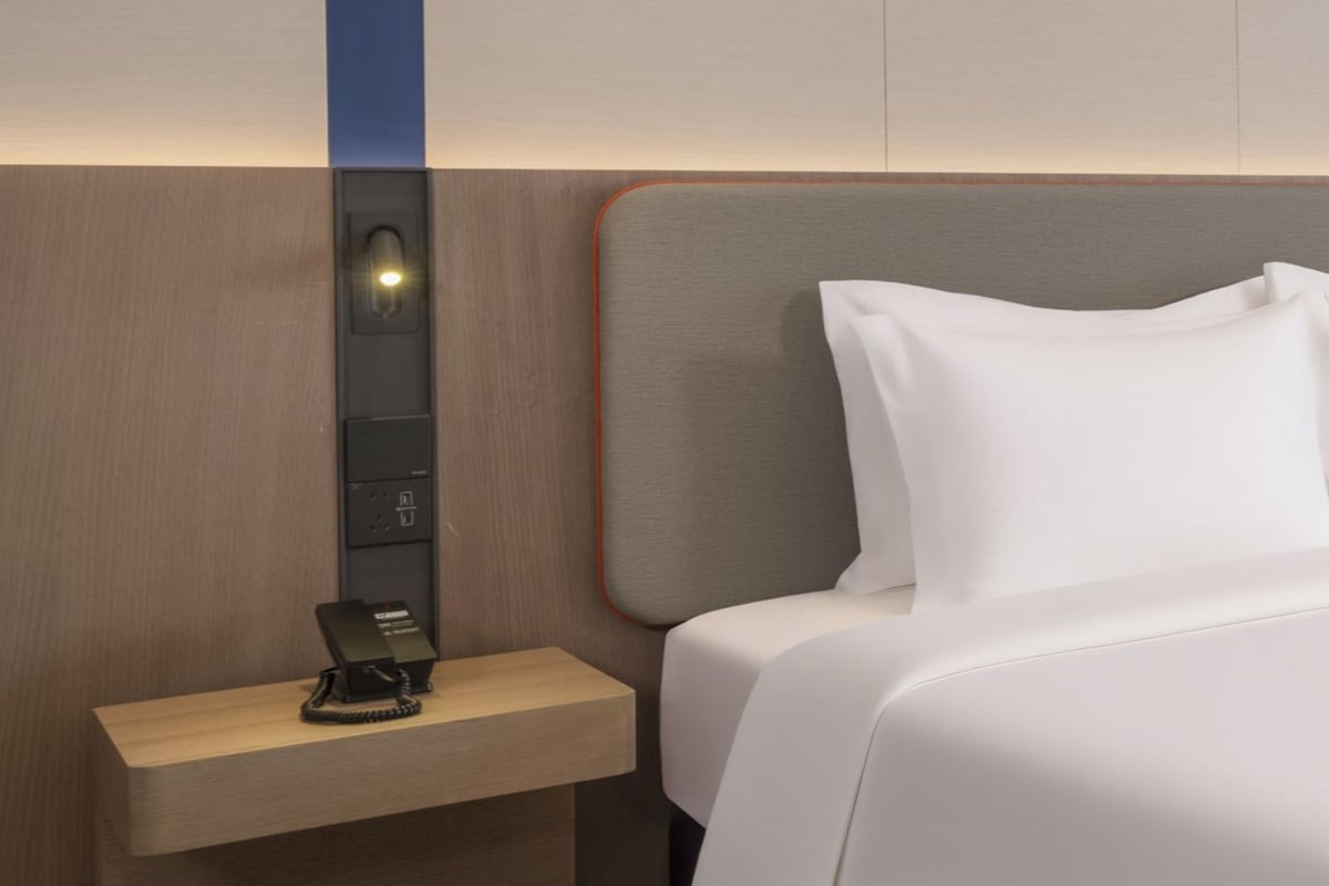A hotel room with a wooden nightstand, a phone, and a bed with white bedding.