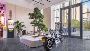 A modern lobby with a motorcycle, a digital information kiosk, seating area, and large windows offering views of high-rise buildings. - Holiday Inn Express Aksu by IHG (Aksu)