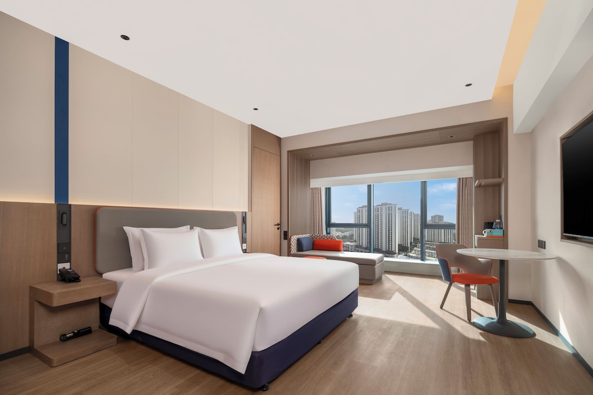 Een moderne hotelkamer met een groot bed, een bureau, een stoel en uitzicht op de stad.