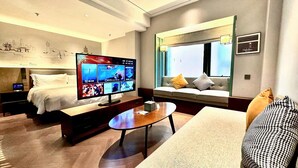 Una habitación de hotel moderna con una televisión de pantalla plana grande, un sofá, una mesa de centro y una cama con una mesita de noche.
