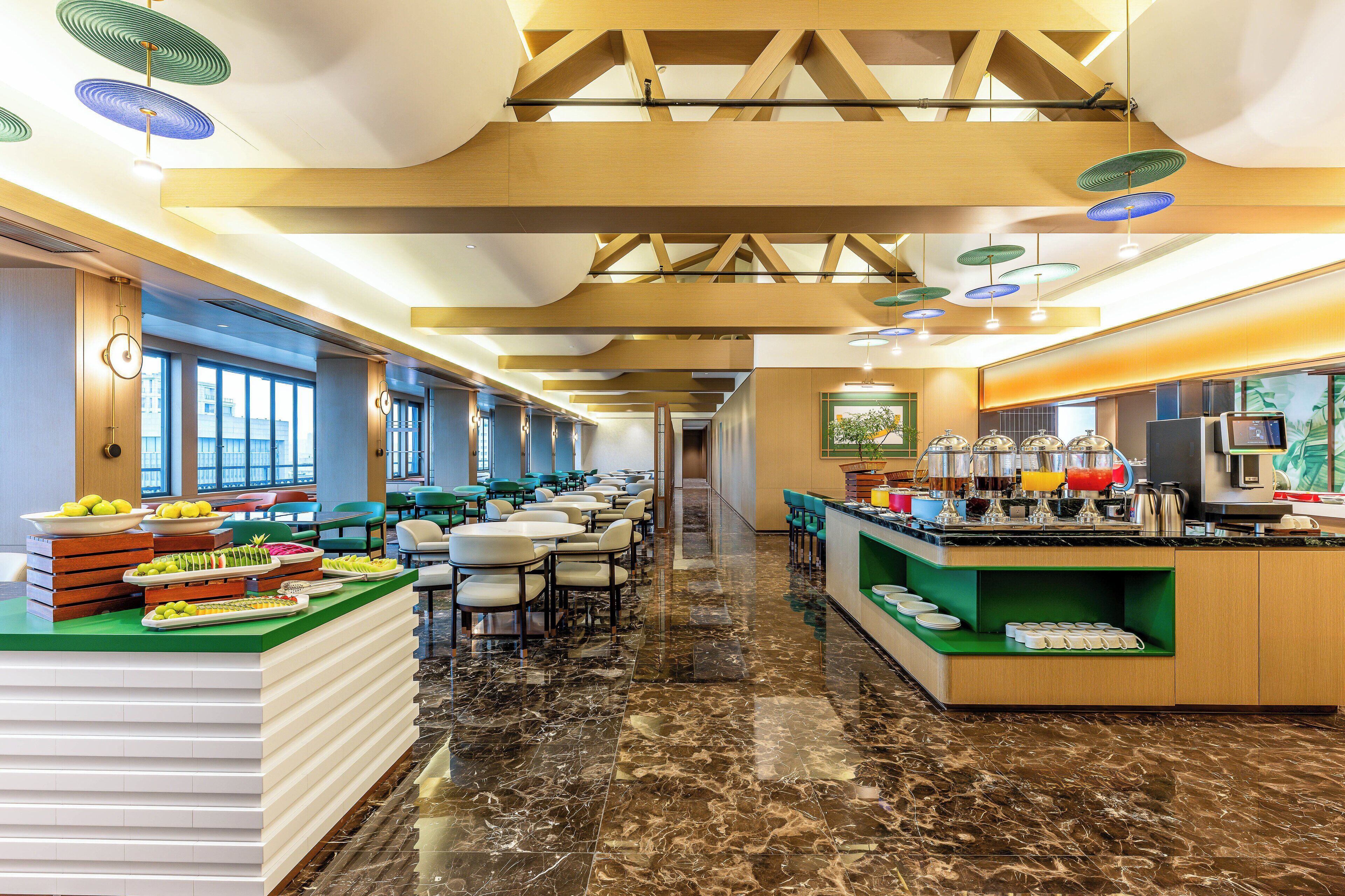 A modern hotel lobby with a marble floor, a buffet area with food, and a seating area with tables and chairs.