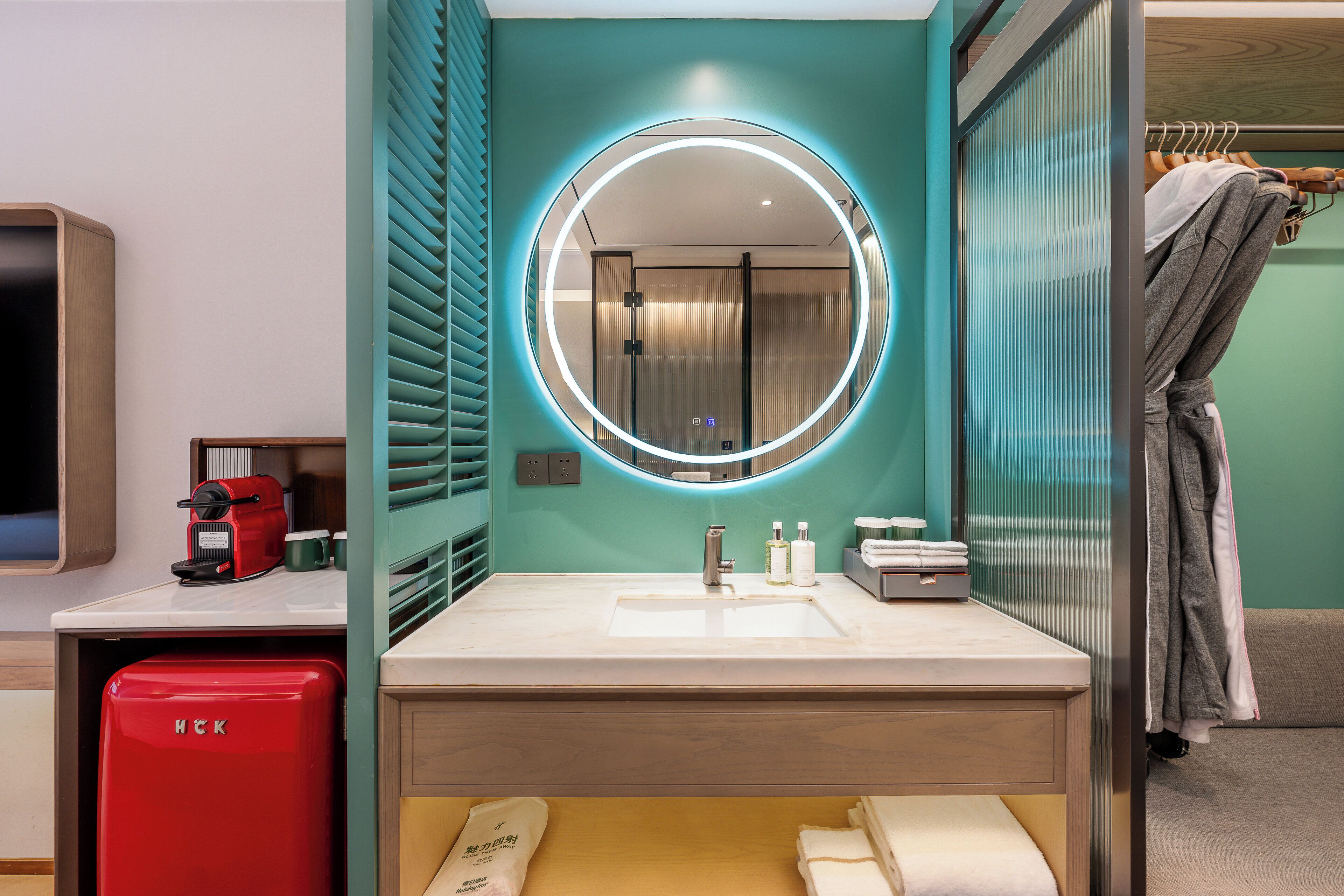 A modern bathroom with a round mirror, sink, and a red appliance.