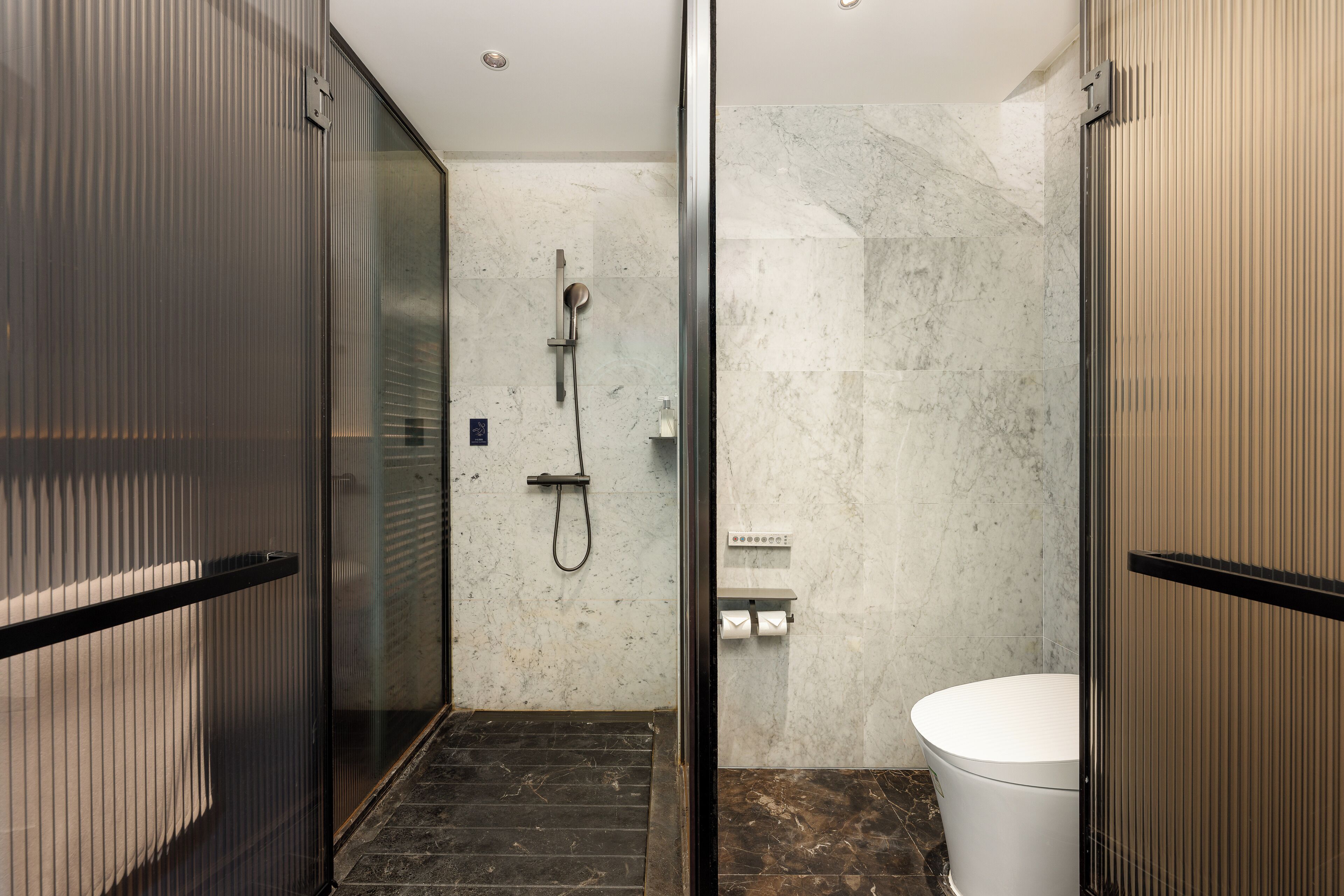 Ein modernes Badezimmer mit einer Duschkabine aus Glas, einer weißen Toilette und einer Wand mit Marmorplatten.
