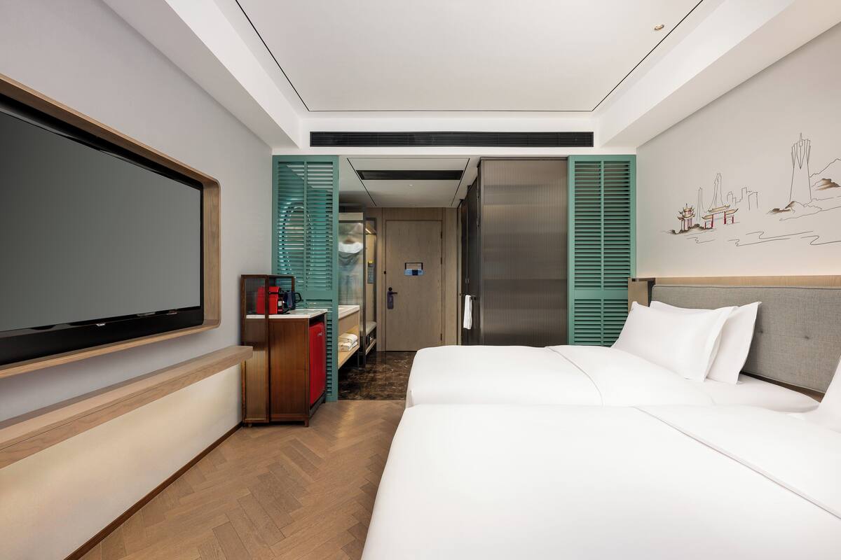 A hotel room with a large bed, a flat-screen TV, a minibar, and a bathroom with a shower and toilet.