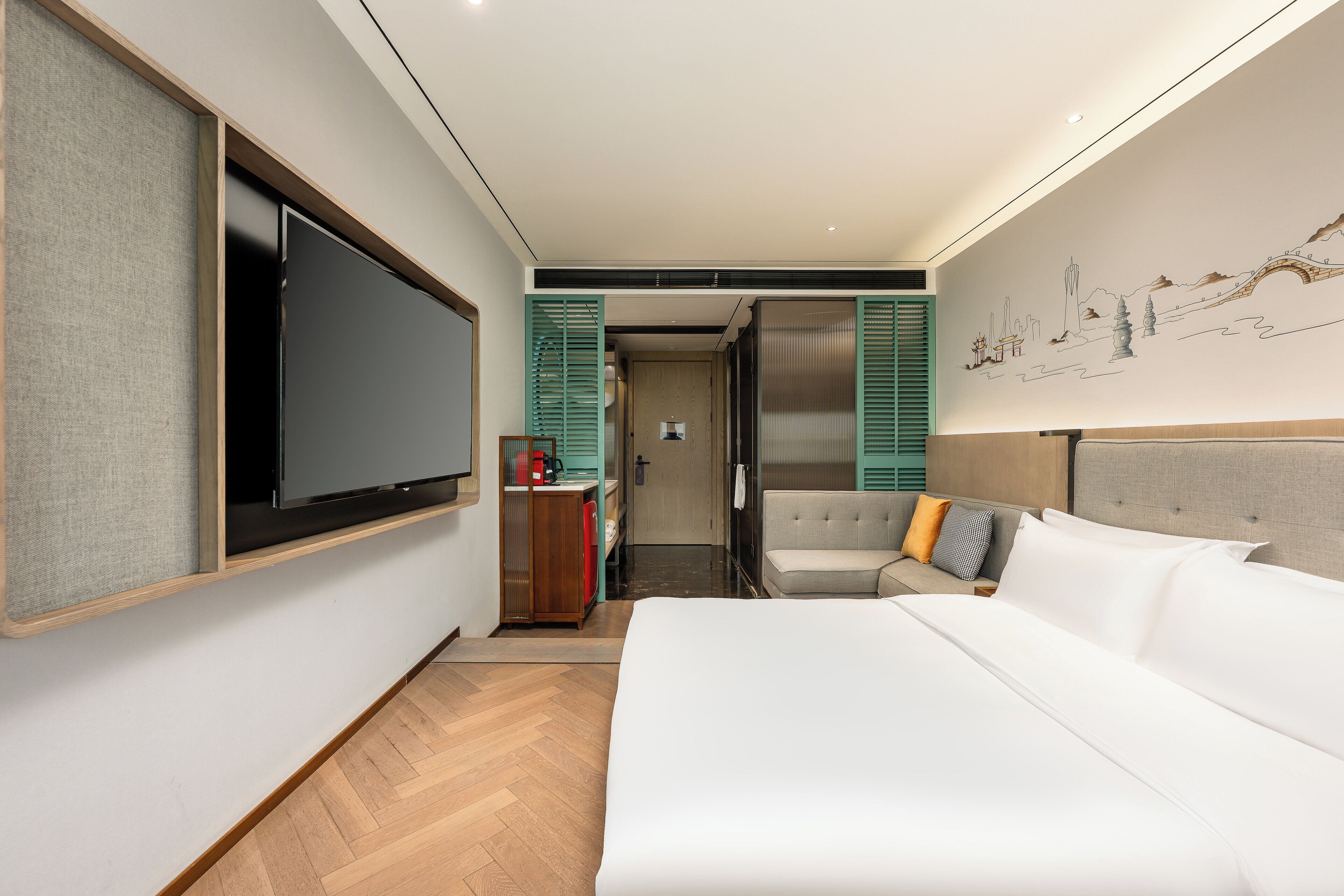 A modern hotel room with a large bed, a flat-screen TV, a sofa, and a wall mural.