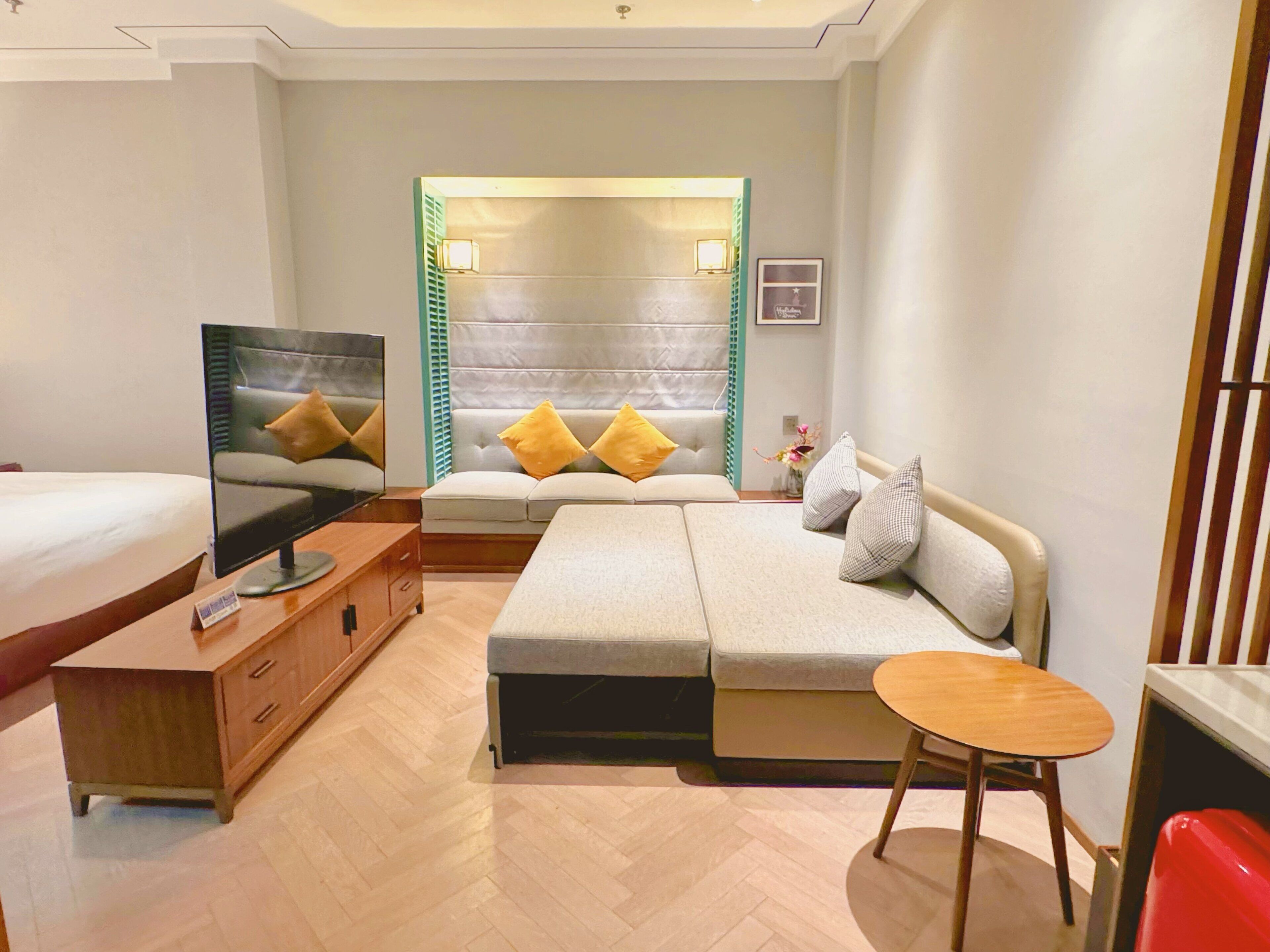 A hotel room with a bed, a sofa, a TV, a wooden dresser, and a small table.