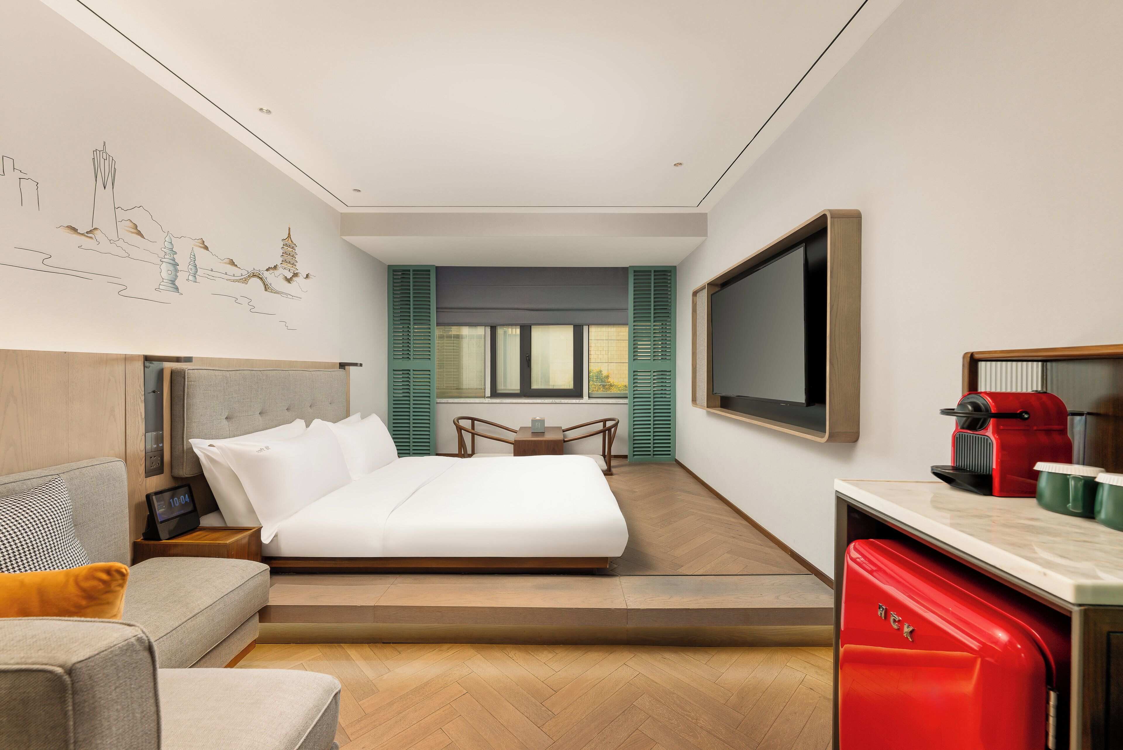 A modern hotel room with a bed, a sofa, a TV, a coffee machine, and a wall art depicting a cityscape.