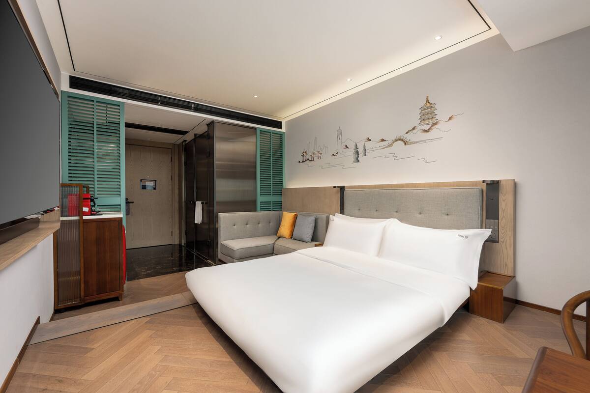A modern bedroom with a large bed, a sofa, a desk, and a wall art piece.