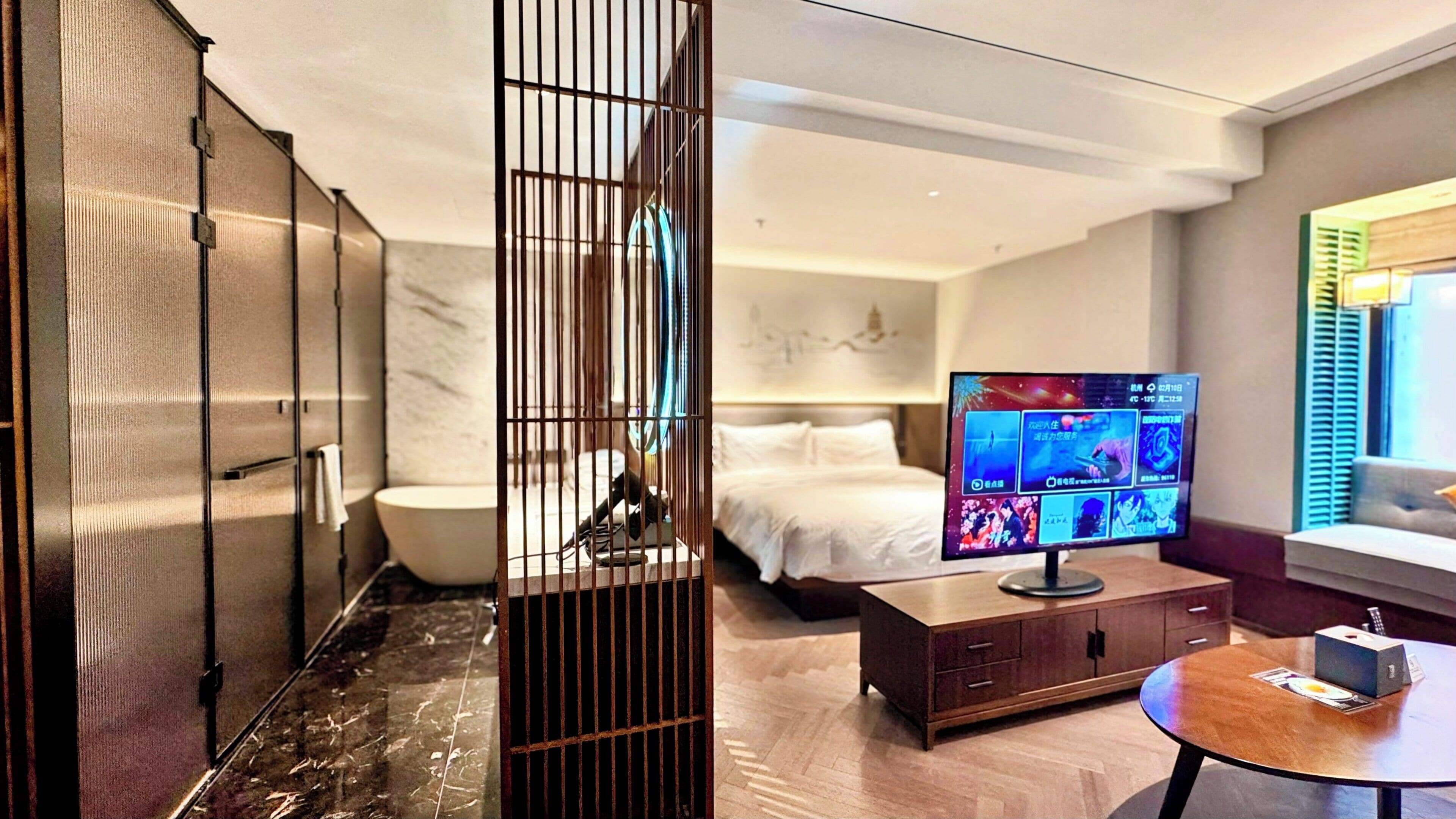A hotel room with a bed, a television, a wooden cabinet, and a window with blinds.