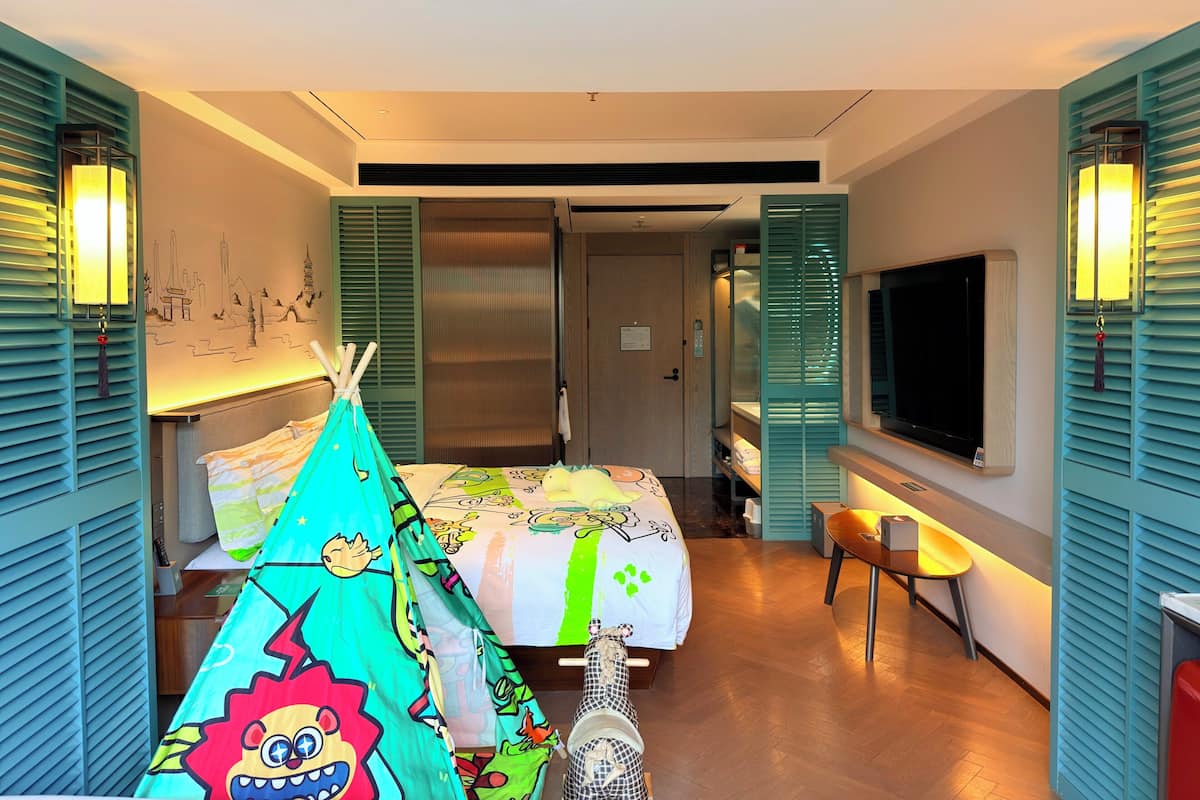 A hotel room with a bed, a tent, a television, and a desk.