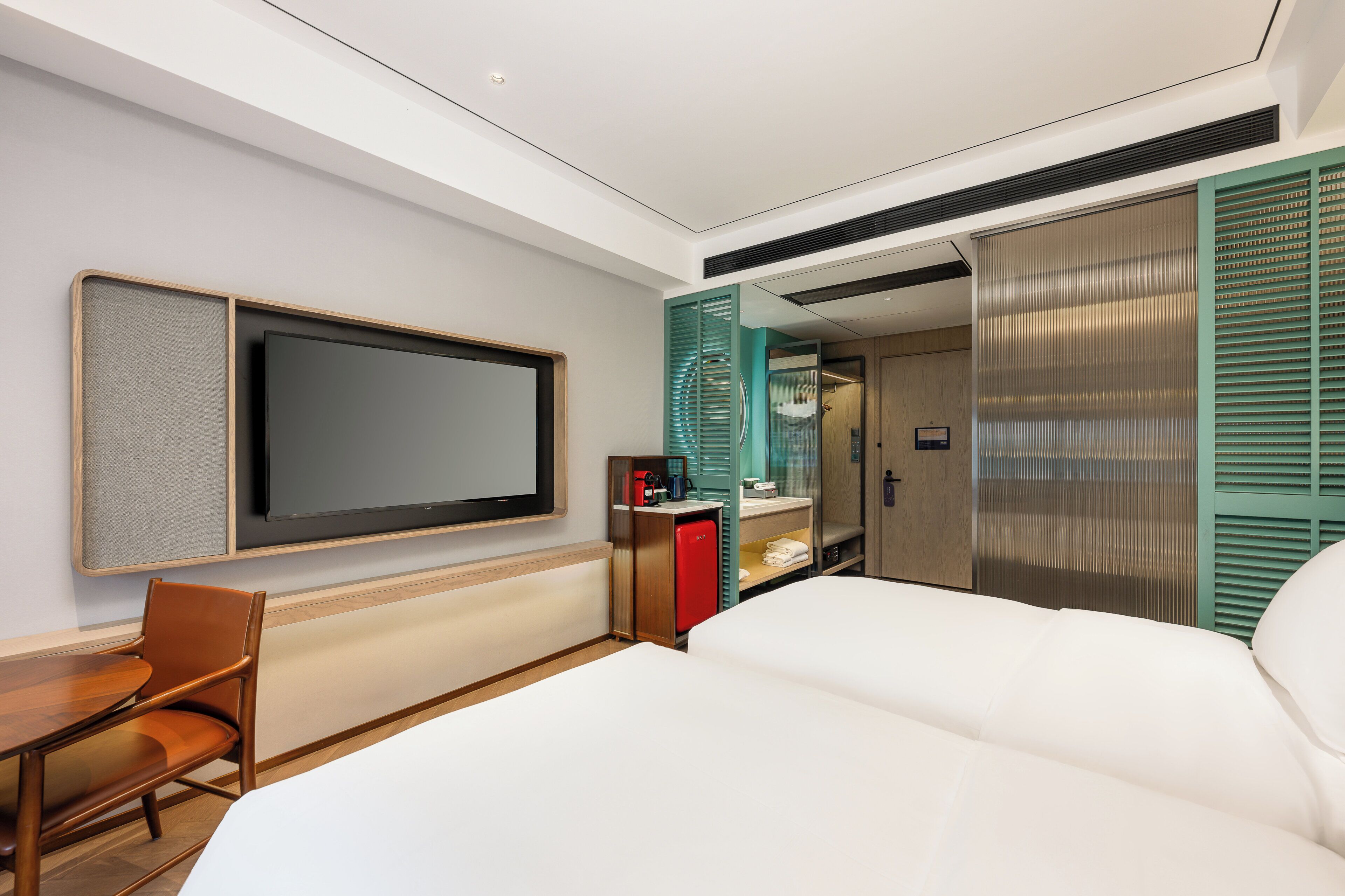 Una moderna camera d'albergo con un ampio letto, una televisione a schermo piatto, una scrivania con una sedia e un mini-frigorifero.