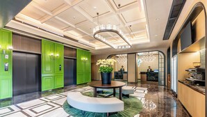 Un vestíbulo moderno con ascensores verde y negro, una mesa redonda con planta en maceta y un mostrador de recepción.