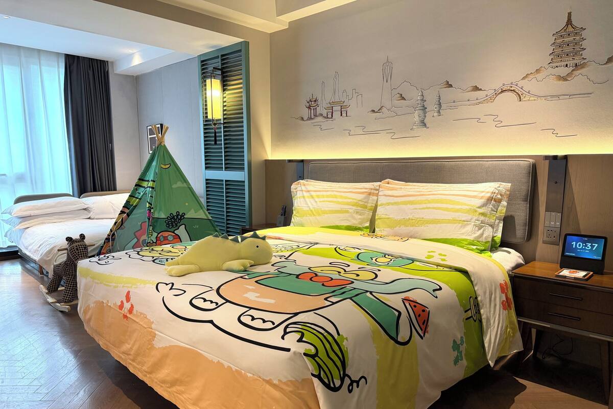 A hotel room with a bed, a nightstand, a digital clock, a wall mural, and a window with curtains.