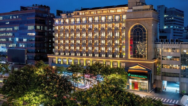 Un hotel de varios pisos con una entrada abovedada destacada y ventanas iluminadas.