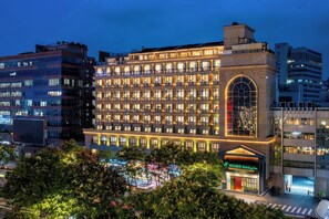 Un hotel de varios pisos con una entrada abovedada destacada y ventanas iluminadas.
