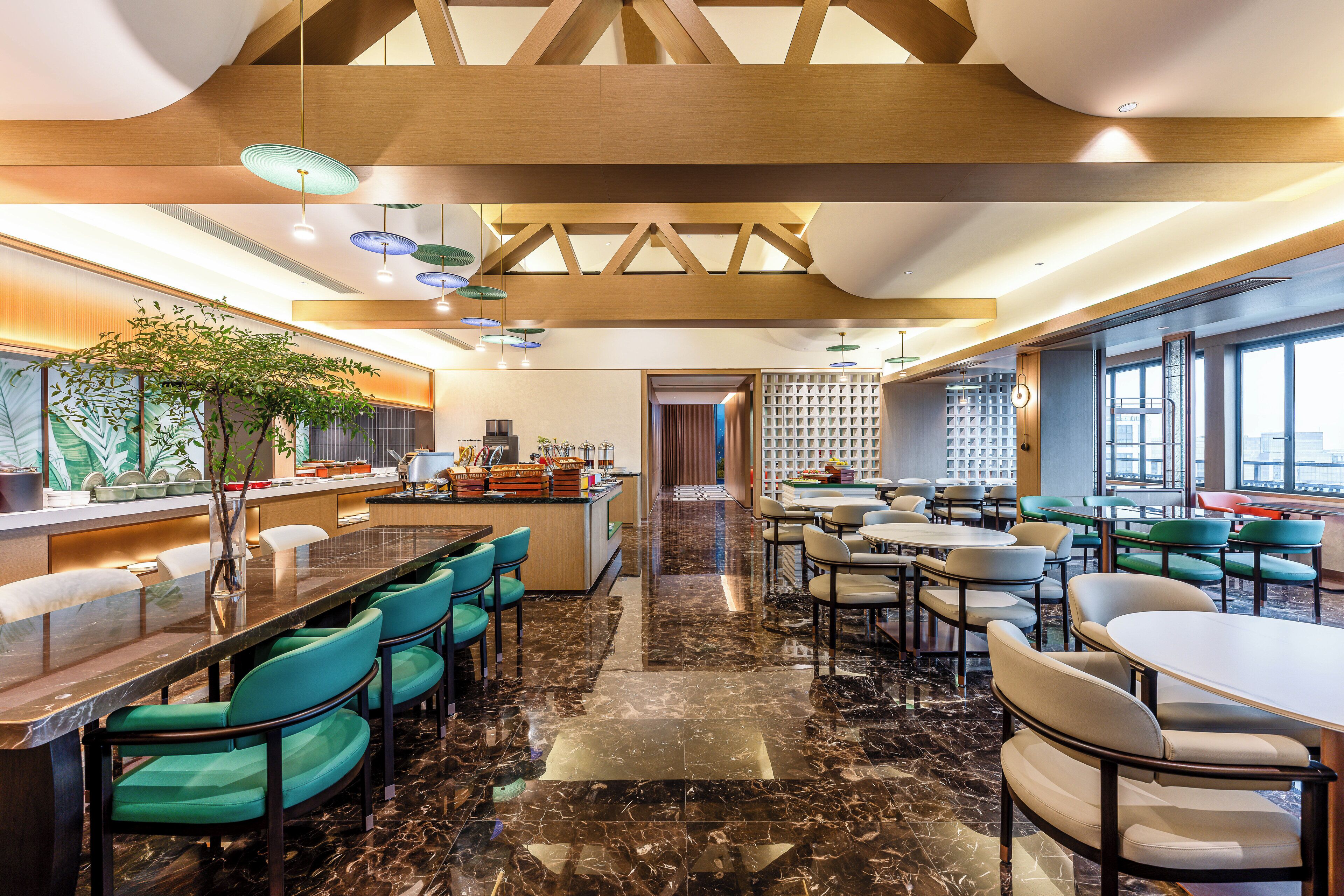 A modern restaurant with a long counter, green chairs, and a marble floor.