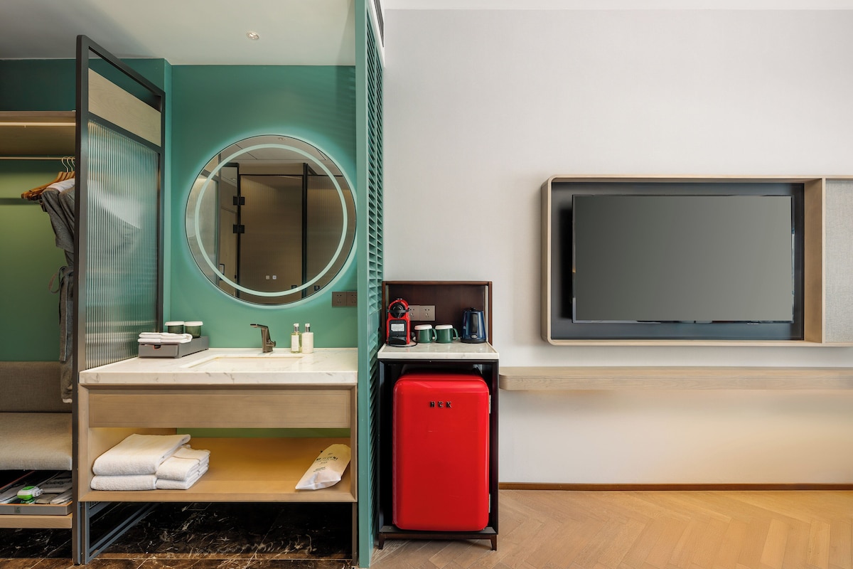 Un baño moderno con lavabo, espejo y un electrodoméstico rojo, probablemente un mini refrigerador o calefactor.