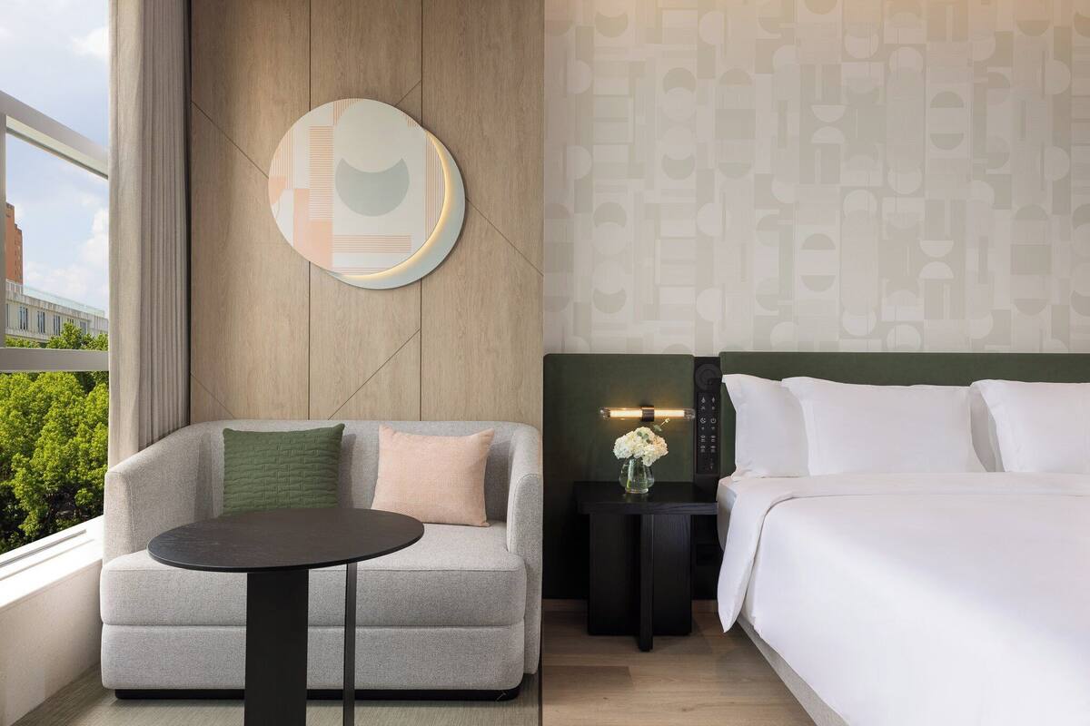 Habitación de hotel con sofá, una mesita, cama, mesita de noche con lámpara y pared con diseño geométrico.