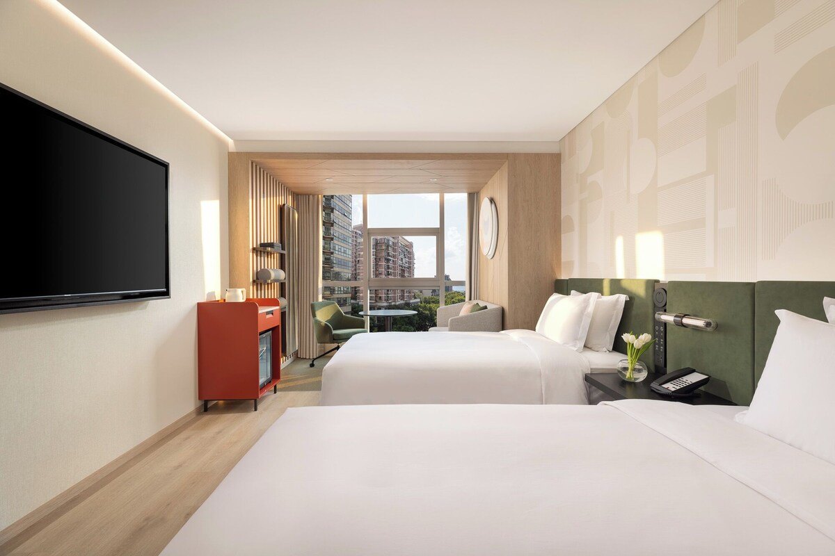 Une chambre d’hôtel avec deux lits, une télévision, un bureau et une vue sur la ville.